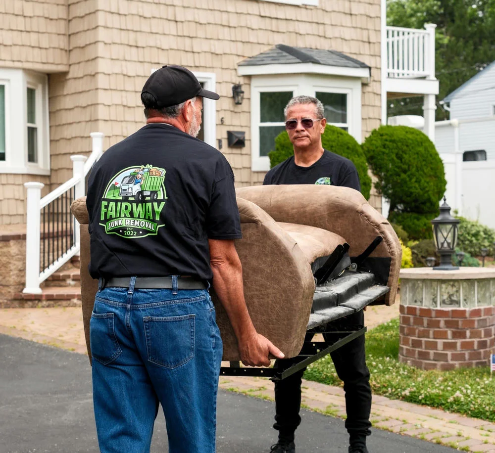 Two men wearing Fairway Junk Removal shirts carry a tan couch out of a house during a junk removal service.